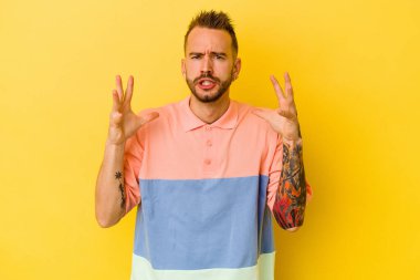 Sarı arka planda izole edilmiş genç dövmeli beyaz adam öfkeyle bağırıyor..