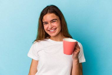 Kafkasyalı genç bir kadın mavi arka planda izole edilmiş bir kupa tutuyor. Mutlu, gülümseyen ve neşeli..