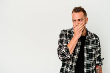 Genç dövmeli beyaz adam beyaz arka planda izole edilmiş. Düşünceli bir şekilde bir fotokopi odasına bakıyor. Ağzını eliyle kapatıyor..