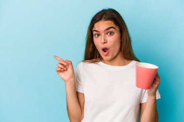 Kafkasyalı genç bir kadın elinde bir kupa tutuyor. Mavi arka planda izole edilmiş. Yan tarafı gösteriyor.
