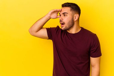 Kafkasyalı genç adam sarı arka planda izole edilmiş, uzaklara bakıyor ve elini alnına koyuyor..