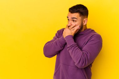 Kafkasyalı genç adam sarı arka planda izole edilmiş. Düşünceli bir şekilde, ağzını eliyle kapatan bir fotokopi odasına bakıyor..