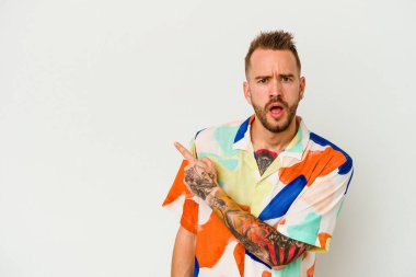 Beyaz arka planda izole edilmiş genç dövmeli beyaz adam yan tarafı işaret ediyor.