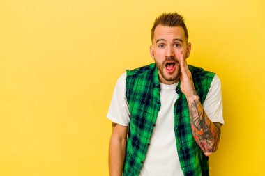 Sarı arka planda izole edilmiş genç dövmeli beyaz adam yüksek sesle bağırıyor, gözleri açık ve elleri gergin tutuyor..
