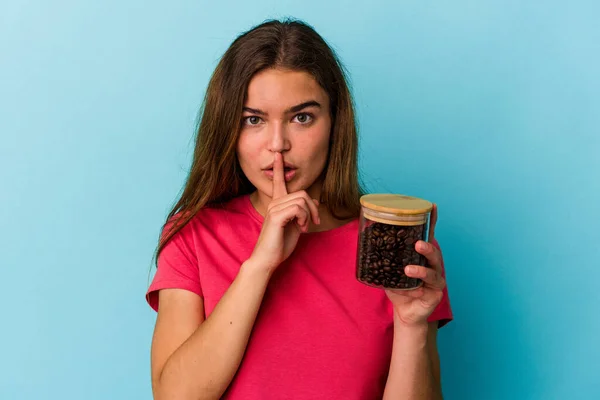 年轻的高加索女人拿着一个用蓝色背景隔开的咖啡壶保守秘密或要求安静 — 图库照片