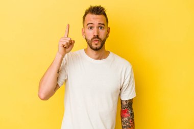 Sarı arka planda izole edilmiş, ağzı açık, üst tarafı gösteren genç dövmeli beyaz adam..