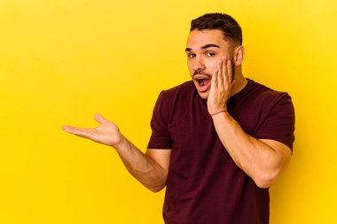 Sarı arka planda izole edilmiş genç beyaz adam, avuç içi fotokopi alanını elinde tutmaktan etkilendi..