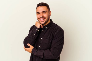 Beyaz arka planda izole olmuş genç beyaz bir adam gülümsüyor ve kendinden emin, çenesine elleriyle dokunuyor..