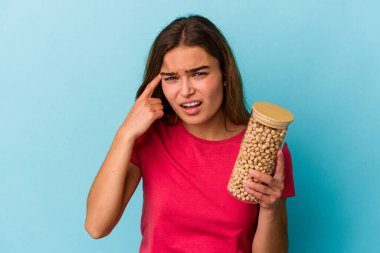 Beyaz arka planda izole edilmiş nohut kavanozu tutan genç beyaz adam işaret parmağıyla bir hayal kırıklığı jesti gösteriyor..