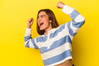 Sarı arka planda izole edilmiş genç beyaz kadın zaferden sonra yumruğunu kaldırıyor, kazanan konsept..