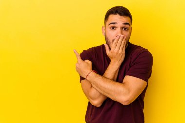Sarı arka planda izole edilmiş genç beyaz adam yan tarafı işaret ediyor.