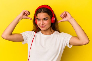 Sarı arka planda izole edilmiş müzik dinleyen genç beyaz kadın gururlu ve kendinden emin hissediyor, örnek olarak.