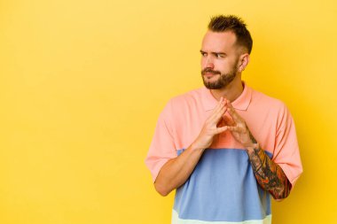 Genç, dövmeli, beyaz bir adam sarı arka planda izole edilmiş bir plan kuruyor..