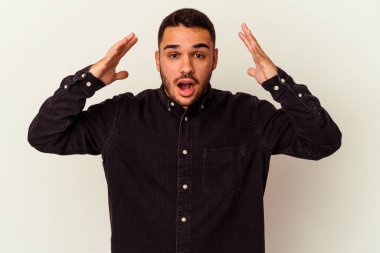 Beyaz arka planda izole olmuş genç beyaz bir adam zaferi veya başarıyı kutluyor, şaşırıyor ve şok oluyor..