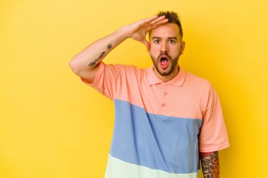 Sarı arka planda izole edilmiş genç dövmeli beyaz adam yüksek sesle bağırıyor, gözleri açık ve elleri gergin tutuyor..