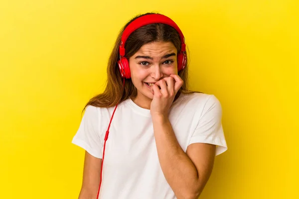 Jovem Caucasiana Ouvindo Música Isolada Fundo Amarelo Mordendo Unhas Nervosa — Fotografia de Stock