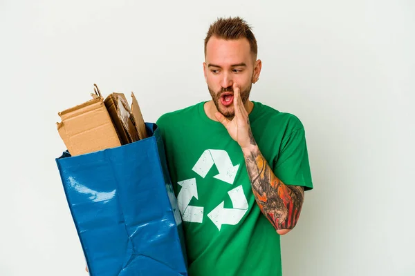 Young caucasian tattooed man recycled cardboard isolated on white background is saying a secret hot braking news and looking aside