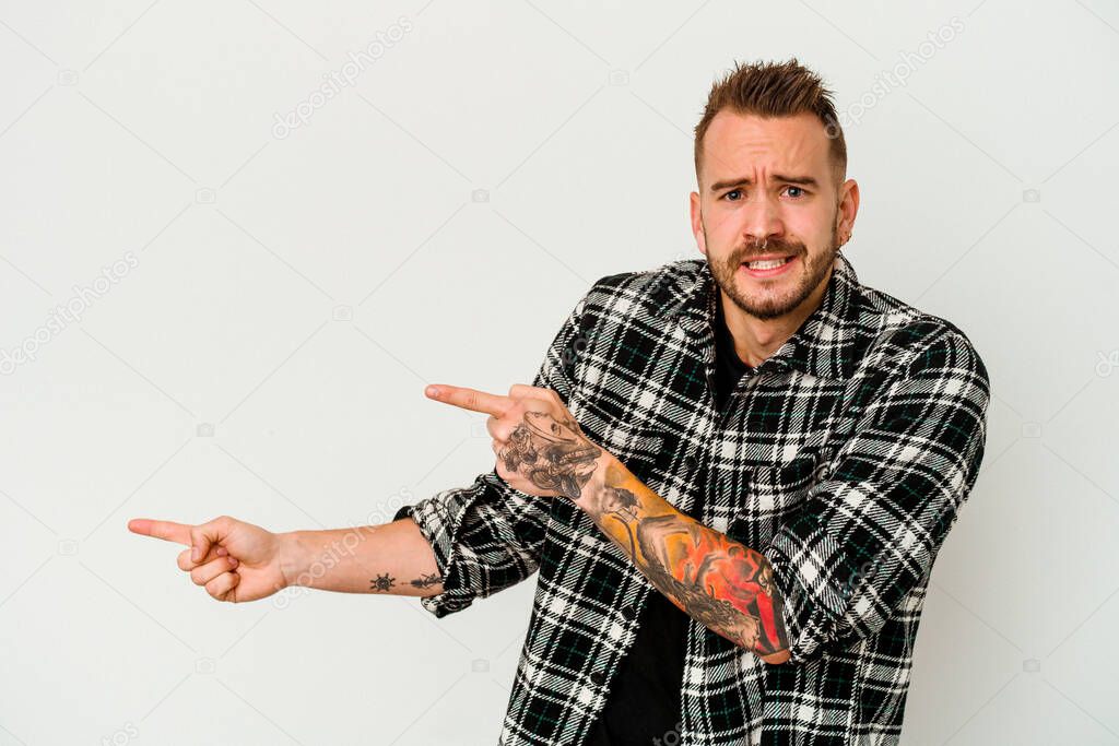 Young tattooed caucasian man isolated on white background shocked pointing with index fingers to a copy space.