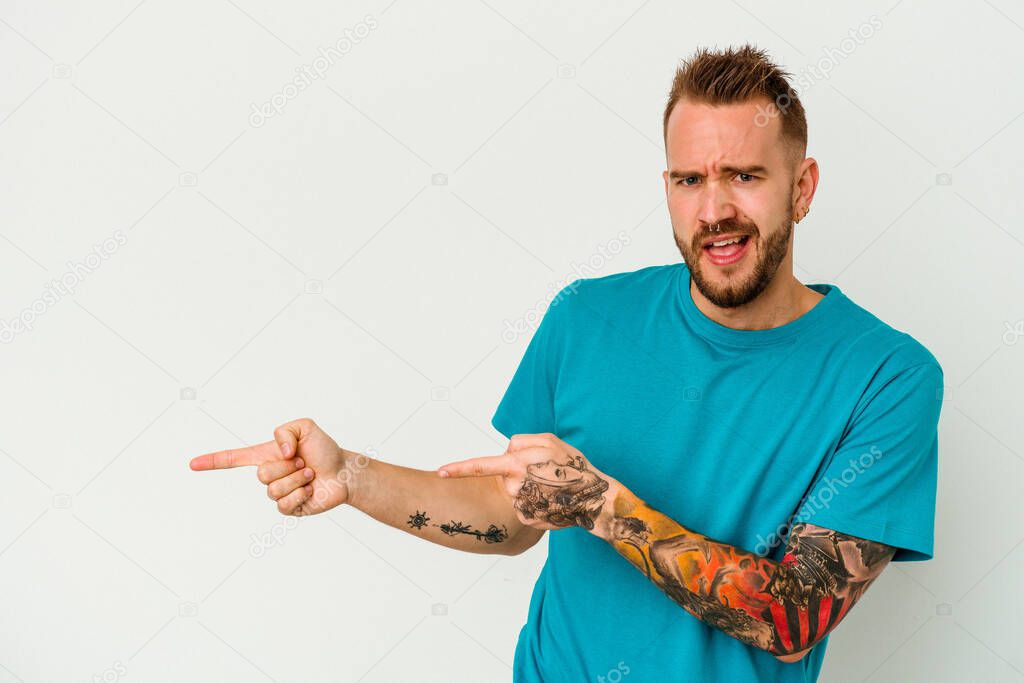 Young tattooed caucasian man isolated on white background pointing with forefingers to a copy space, expressing excitement and desire.