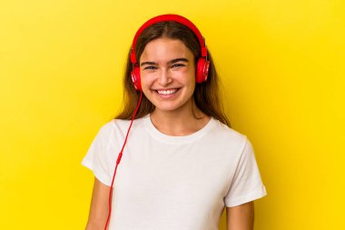 Sarı arka planda izole edilmiş müzik dinleyen genç beyaz kadın mutlu, güler yüzlü ve neşeli..
