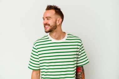 Beyaz arka planda izole edilmiş genç dövmeli beyaz adam mutlu bir şekilde gülüyor ve ellerini karnının üstünde tutarak eğleniyor..