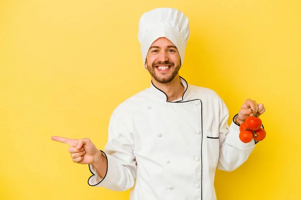 Mladý Kavkazský Kuchař Drží Rajčata Izolovaná Žlutém Pozadí Usmívá Ukazuje — Stock fotografie