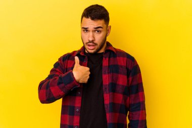Sarı arka planda izole edilmiş genç beyaz adam parmağını göstererek şaşırdı ve gülümsedi..
