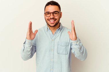 Beyaz arka planda izole edilmiş genç beyaz bir adam işaret parmaklarıyla küçük bir şey tutuyor, gülümsüyor ve kendinden emin..