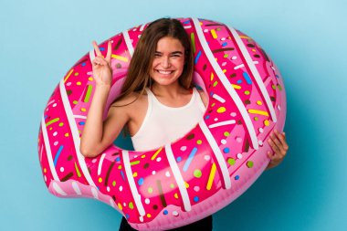 Mavi arka planda izole edilmiş şişme donutu olan beyaz bir kadın iki numarayı parmaklarıyla gösteriyor..