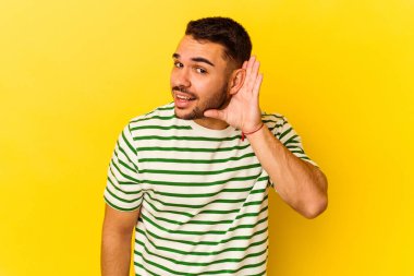Sarı arka planda izole edilmiş genç beyaz bir adam bir dedikoduyu dinlemeye çalışıyor..