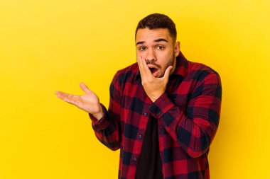 Sarı arka planda izole edilmiş genç beyaz bir adam bir avuç içinde fotokopi alanı tutuyor, el üstünde tutuyor. Şaşırmış ve mutlu..