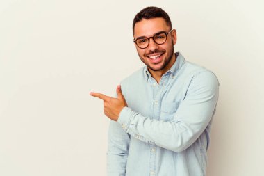 Beyaz arka planda izole edilmiş genç beyaz bir adam gülümsüyor ve boş alanda bir şeyler gösteriyor..