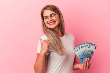 Pembe arka plan noktalarına izole edilmiş banknotlar tutan genç Rus kadın başparmak uzakta, gülüyor ve kaygısız..