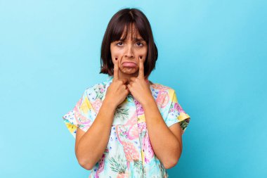 Genç melez kadın mavi arka planda izole edilmiş, ağlıyor, bir şeyden mutsuz, acı ve kafa karışıklığı konsepti..