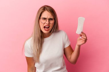 Pembe arka planda izole edilmiş kompres tutan genç Rus kadın çok sinirli ve agresif çığlıklar atıyor..