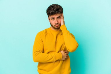 Mavi arka planda izole edilmiş genç beyaz adamın yanakları şişer, yorgun bir ifadesi vardır. Yüz ifadesi kavramı.