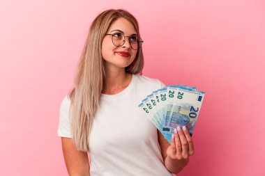 Genç Rus kadın pembe arka planda izole edilmiş banknotlar tutuyor. Amaçlarına ve amaçlarına ulaşma hayali kuruyor.