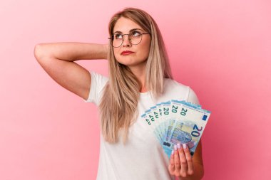 Elinde pembe arka planda izole edilmiş banknotlar tutan genç Rus kadın kafasının arkasına dokunuyor, düşünüyor ve bir seçim yapıyor..