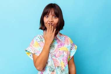 Mavi arka planda izole edilmiş genç bir ırk kadını şok olmuş, ağzı ellerle kaplanmış, yeni bir şey keşfetmeye hevesli..