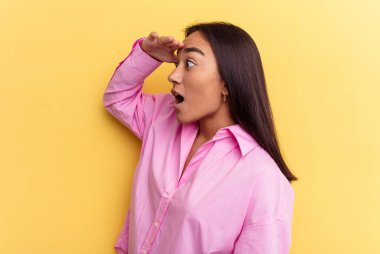 Genç melez kadın, sarı arka planda izole edilmiş. Uzağa bakıyor, elini alnına koyuyor..