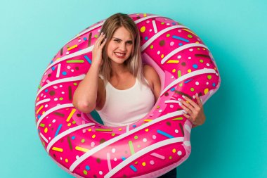 Şişme donutlu genç Rus kadın mavi arka planda izole edilmiş kulakları elleriyle kapatıyor..