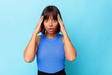 Mavi arka planda izole edilmiş genç melez kadın zaferi ya da başarıyı kutluyor, şaşırıyor ve şok oluyor..