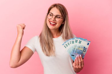 Pembe arka planda izole edilmiş banknotlar tutan genç Rus kadın zaferden sonra yumruğunu kaldırıyor, kazanan konsept..