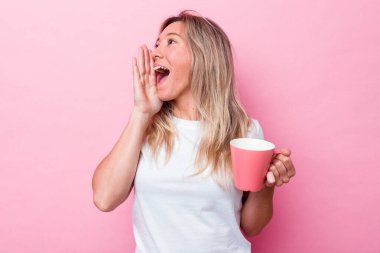 Pembe bir kupa tutan genç Avustralyalı kadın pembe arka planda izole edilmiş bağırıyor ve avuç içini açık tutuyor..