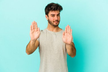 Mavi arka planda izole edilmiş genç beyaz adam elini uzatmış, dur işareti göstererek seni engelliyor..