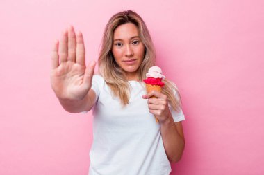 Genç Avustralyalı bir kadın pembe arka planda izole edilmiş bir dondurma tutuyor elini uzatmış, dur işareti gösteriyor ve seni engelliyor..