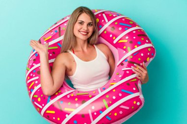 Mavi arka planda izole edilmiş şişme donutlu genç bir Rus kadın bir avuç içinde fotokopi alanı ve belinde başka bir el tutuyor..