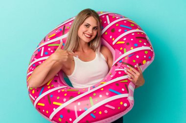 Şişme donutu olan genç Rus kadın mavi arka planda izole edilmiş gömlek fotokopi alanını gösteren, gururlu ve kendinden emin.