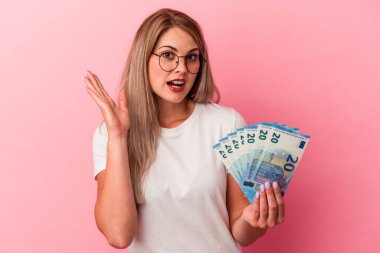 Elinde banknotlar tutan genç Rus kadın pembe arka planda izole edilmiş, şaşırmış ve şok olmuş..