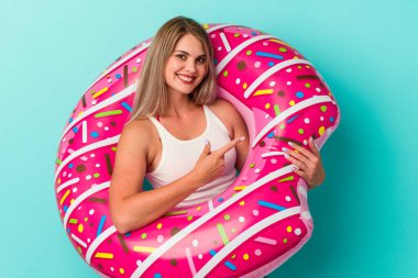 Şişme donutlu genç Rus kadın mavi arka planda izole edilmiş gülümsüyor ve boş alanda bir şeyler gösteriyor..